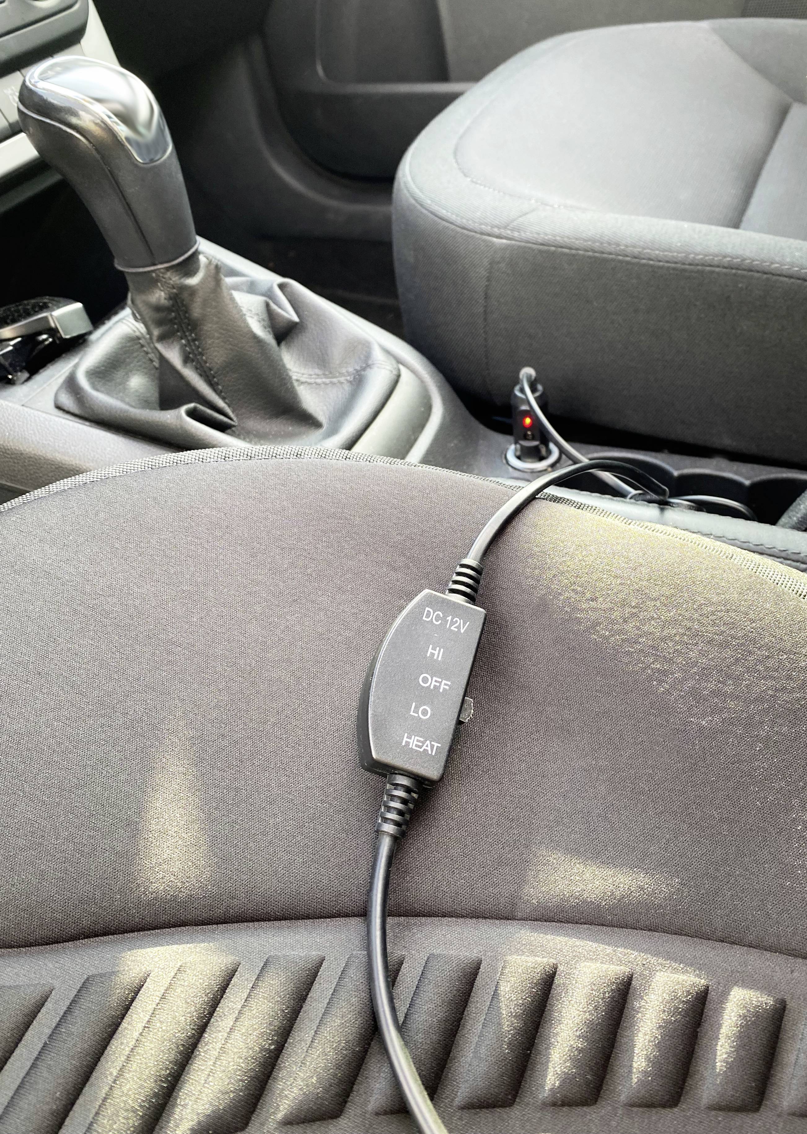 A seat heating controller with settings 'HI', 'OFF', 'LO', and 'HEAT' is lying on a car seat, near a gear lever.