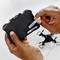 A person inserts two AA batteries into the remote control of a toy drone. The drone is visible in the background.