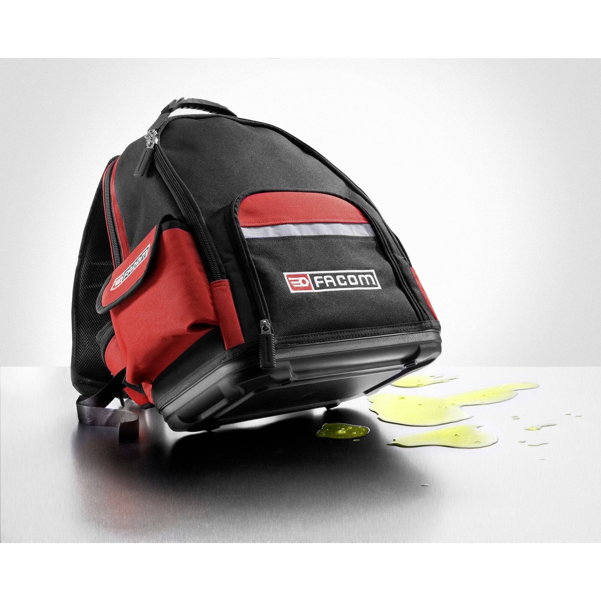 A black and red tool rucksack sits on a table with a yellow liquid beside it.