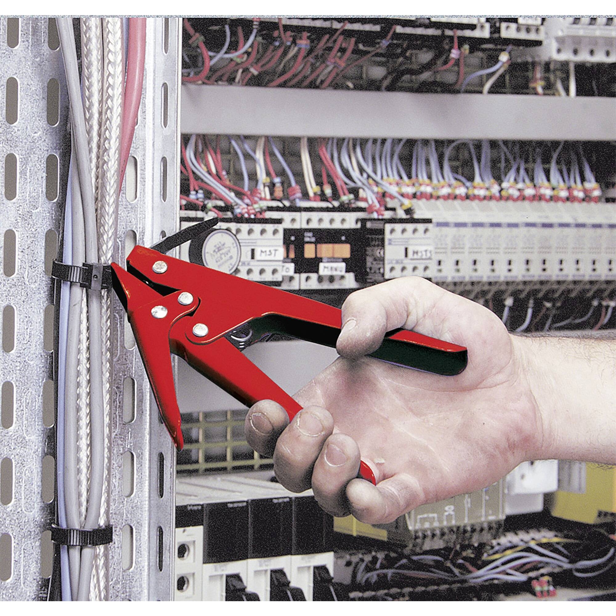 A hand is using a red tool to secure cables. In the background, an open electrical cabinet with visible cables and components.