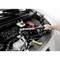 A person is tightening a screw in the engine bay of a car using a torque wrench. The engine bay is open and well-lit.