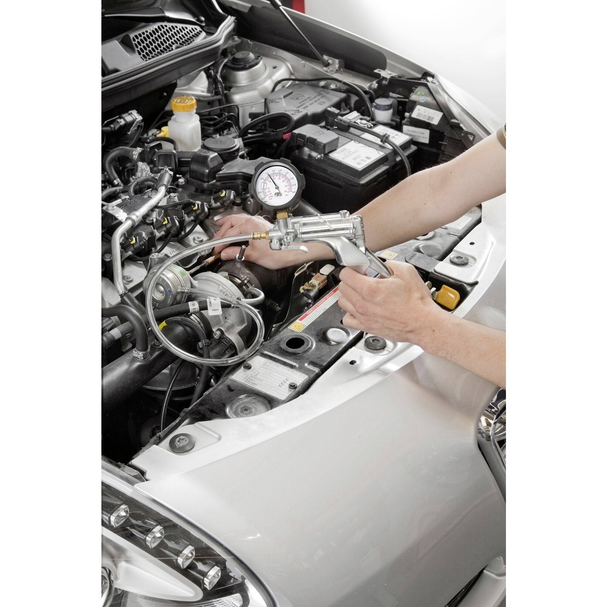 A mechanic is using an air pump with a pressure gauge to check the cooling system in a car. The bonnet is open.