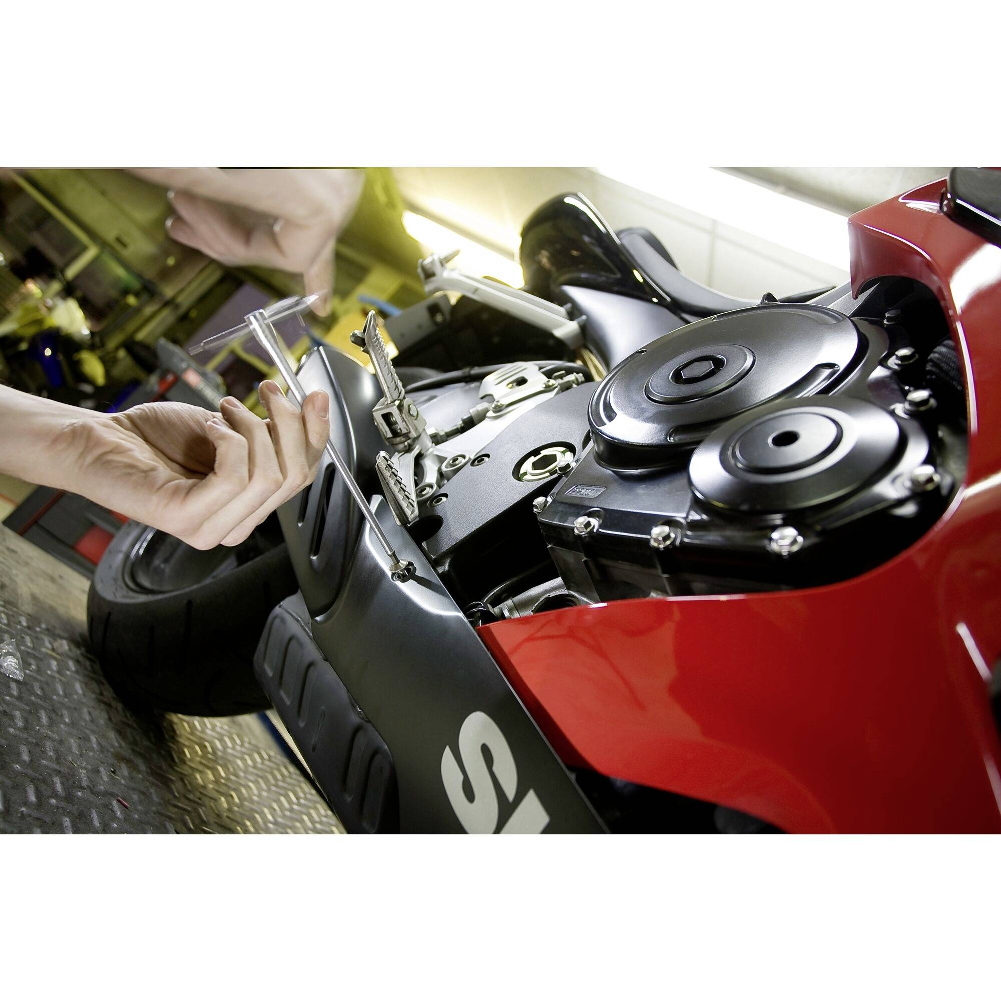 A person is carrying out maintenance work on a motorbike. Their hand is holding a tool, and the engine block is partially open.