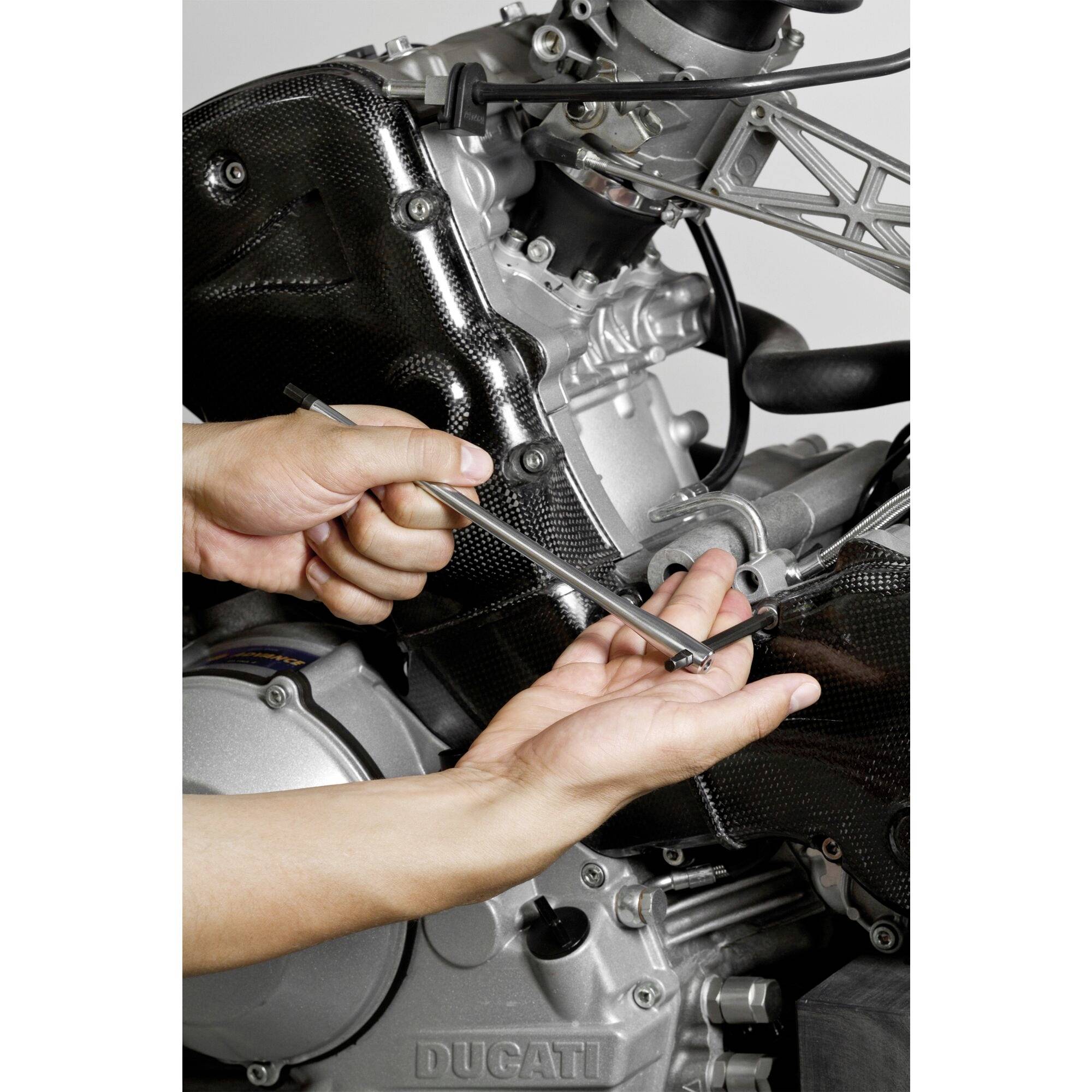 A person is repairing a motorcycle engine with a spanner, their hands positioned close to the engine block.