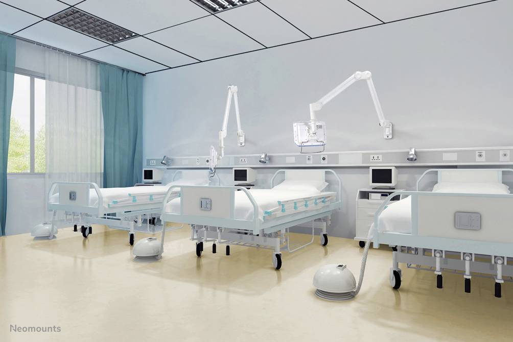 Two empty hospital beds in a bright, modern patient room with medical equipment and monitors on the walls.