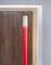 A wooden rod, partially painted red, stands upright against a wall and is enclosed by a metal frame.