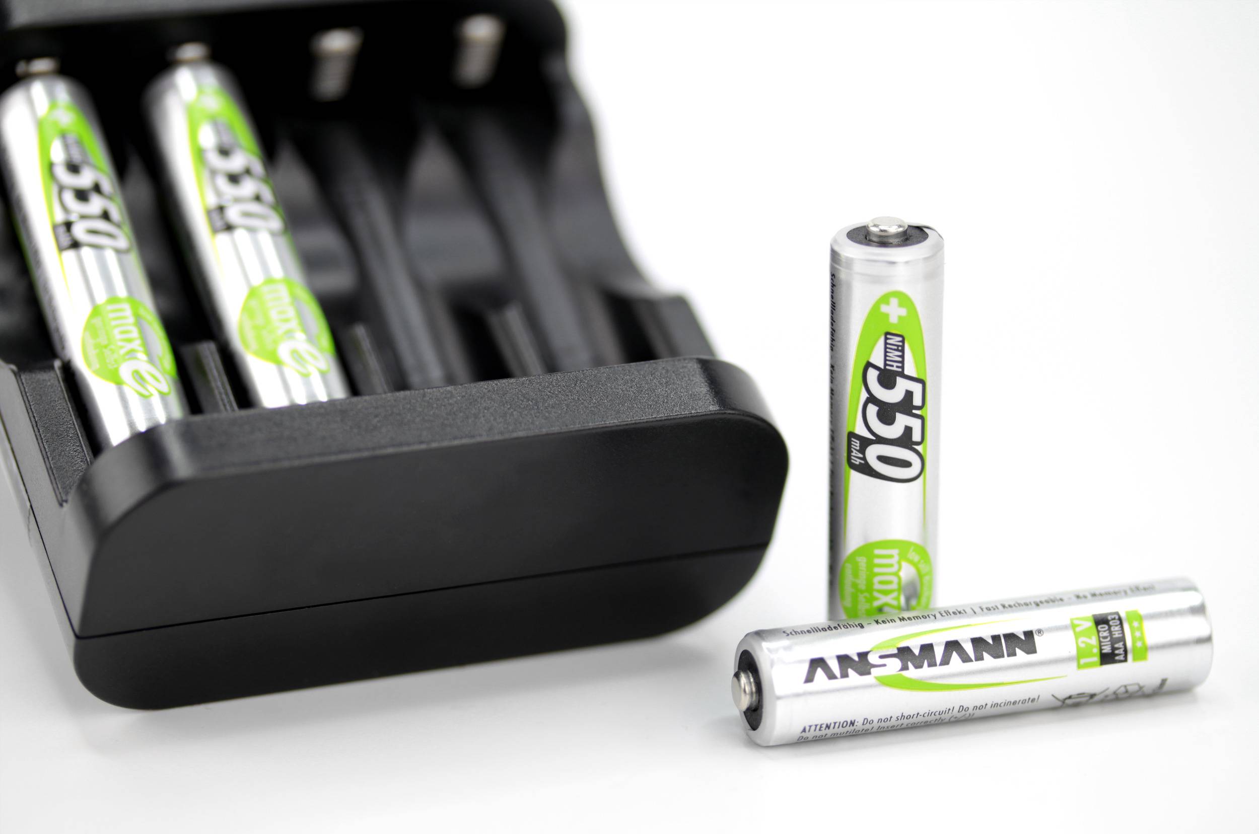 A charger with two AA batteries inserted and two removed batteries placed in front of it on a white surface.