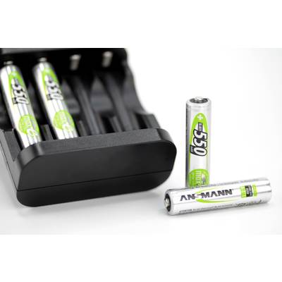 A charger with two AA batteries inserted and two removed batteries placed in front of it on a white surface.