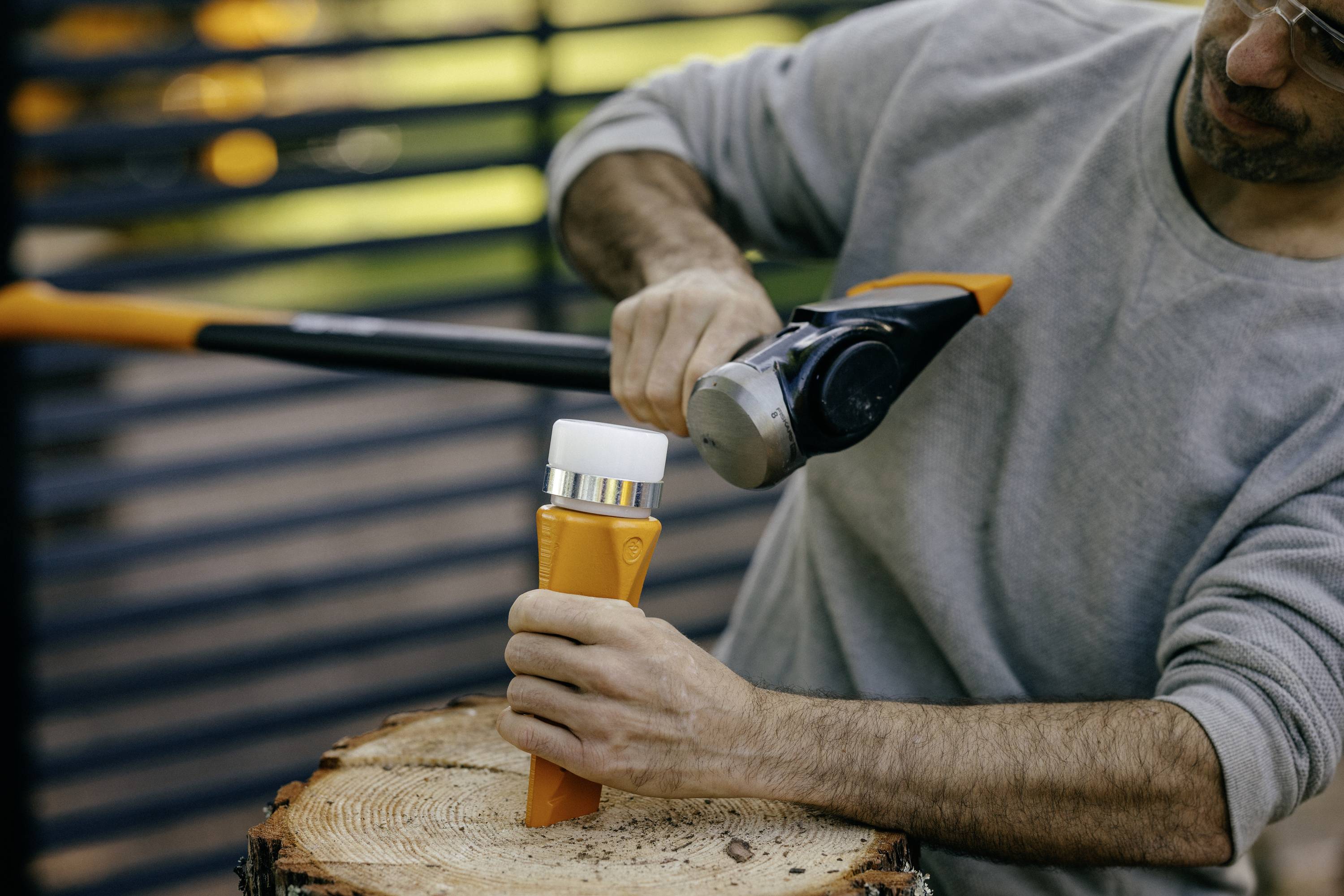 A person is splitting wood with a hammer and wedge on a tree stump. The focus is on the handling of the tool.