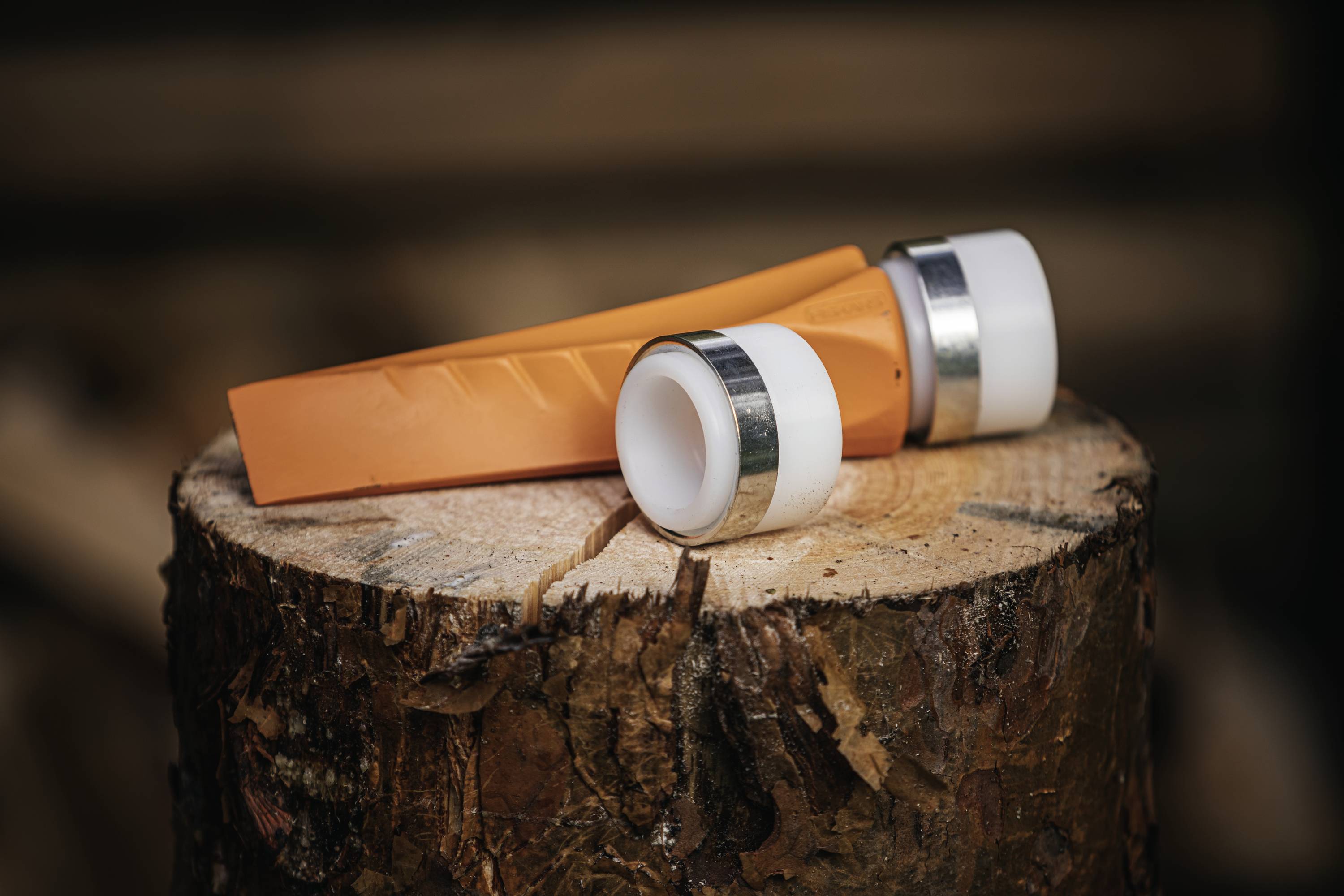 A hunting knife with a white plastic handle and silver blade lies on a tree stump outdoors.