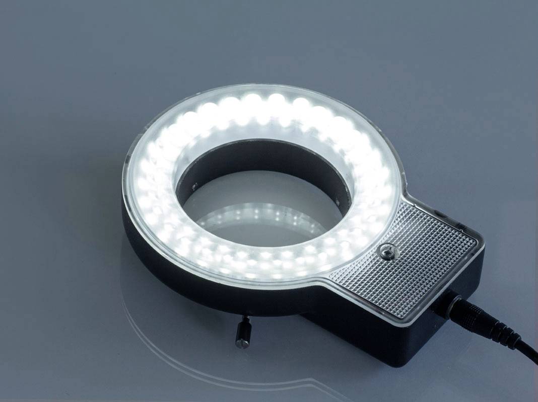 LED ring light on a grey background, switched on and brightly illuminated, with power cable on the right side.