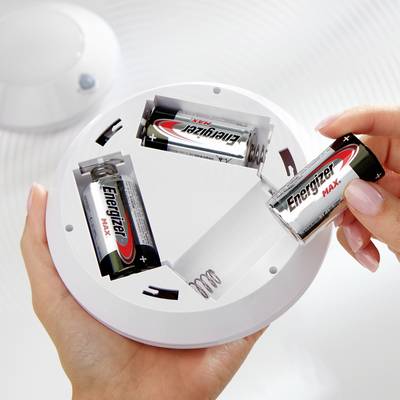 Two hands are holding a smoke detector with batteries being inserted. The batteries, partially removed, bear the 'Energizer' logo.