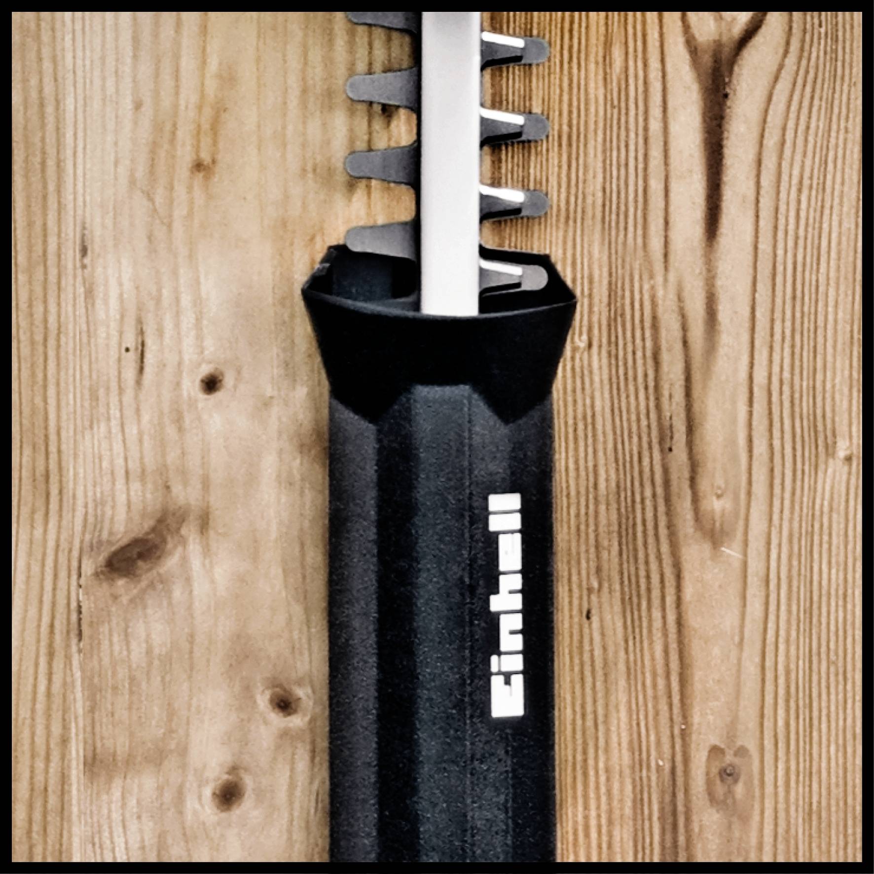 A close-up of an electric cutting tool with a distinctive black handle and 'Einhell' logo. Wooden background.