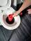 A hand is using a red plunger to unblock a toilet. The scene takes place in a bathroom with dark tiles.