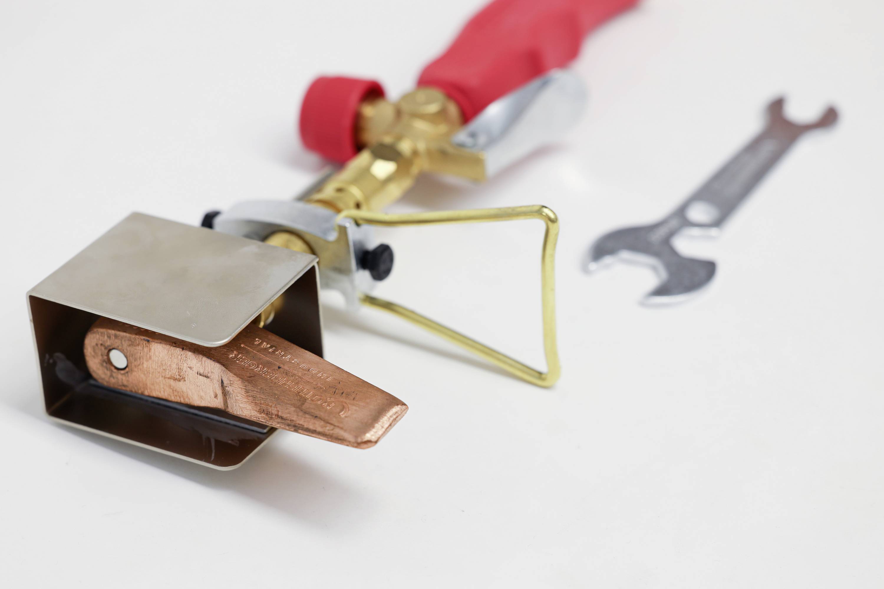 Blow torch on a white background with a red handle and an adjustable gas nozzle. A spanner lies beside it.