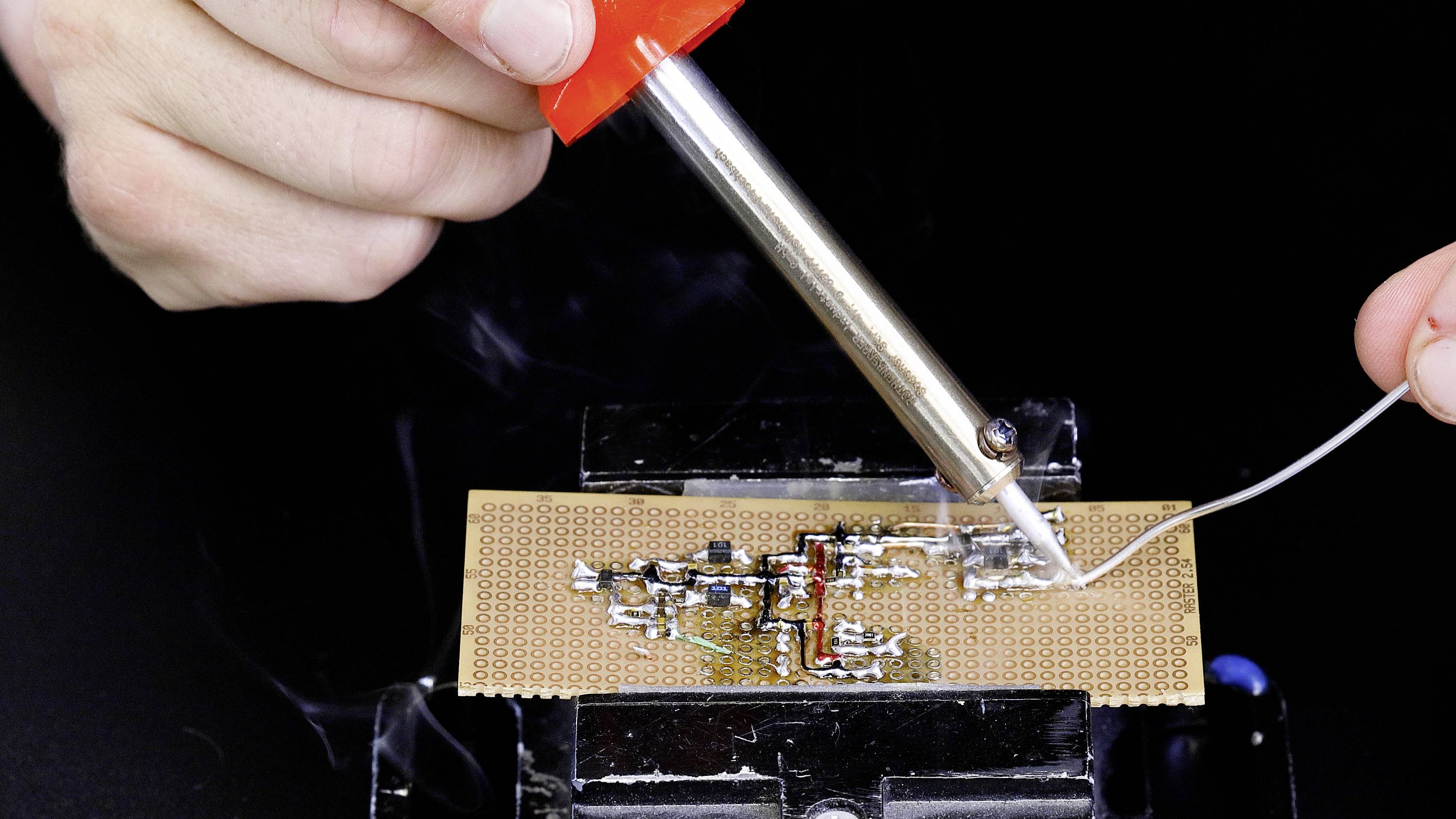 A person is soldering on a circuit board with a soldering iron. One hand is holding the solder, while the soldering iron drips it onto the contacts.