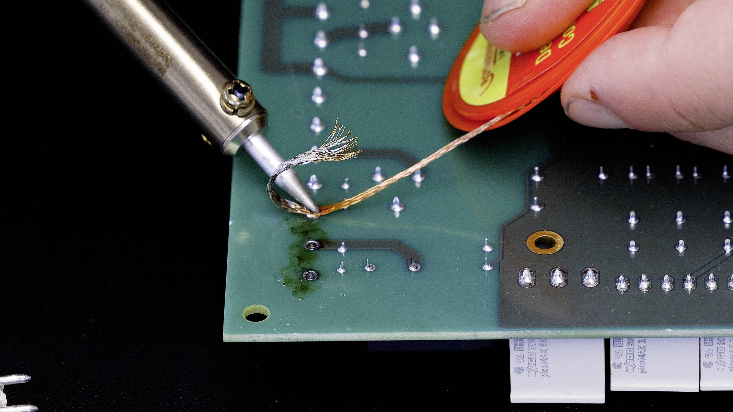 A circuit board is worked on with a soldering iron and solder to remove or correct soldered connections.