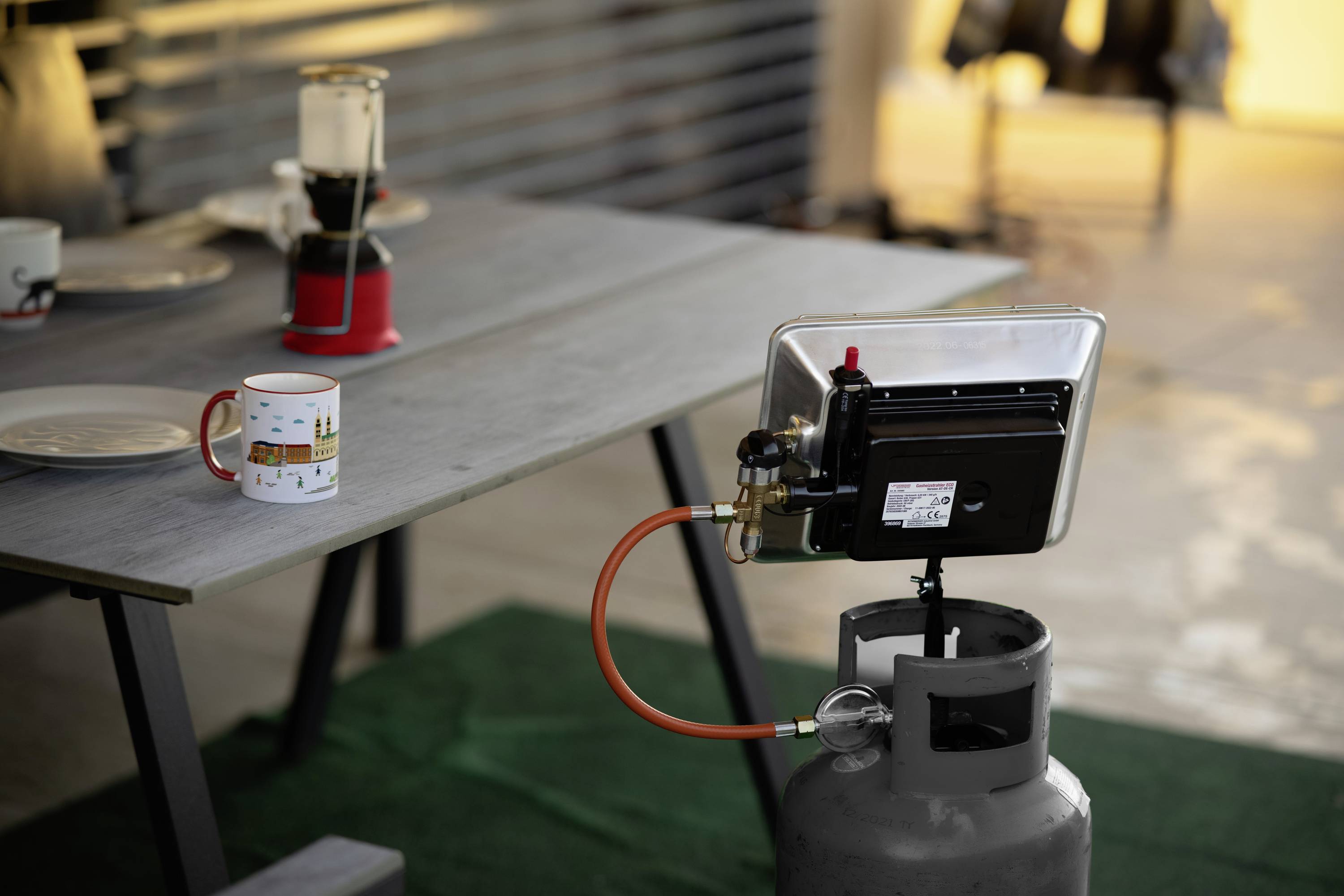 A gas stove is positioned on a gas cylinder beside a table with crockery in an outdoor area, ready for cooking.