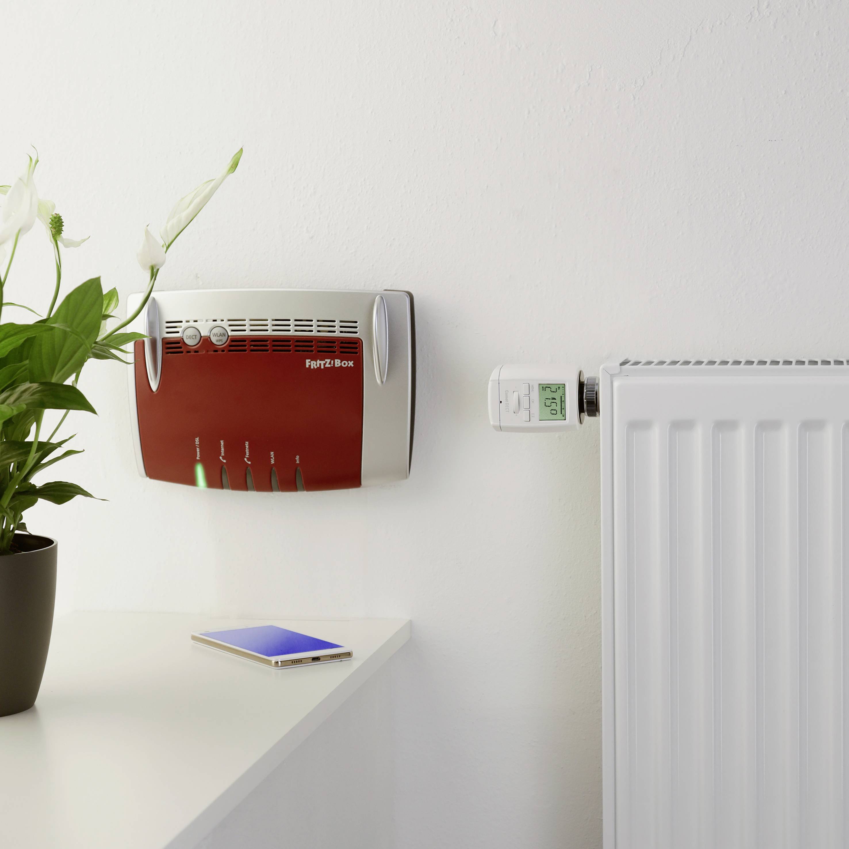 A Wi-Fi router is mounted on the wall next to a thermostat on a radiator. A plant sits on the table beside it.