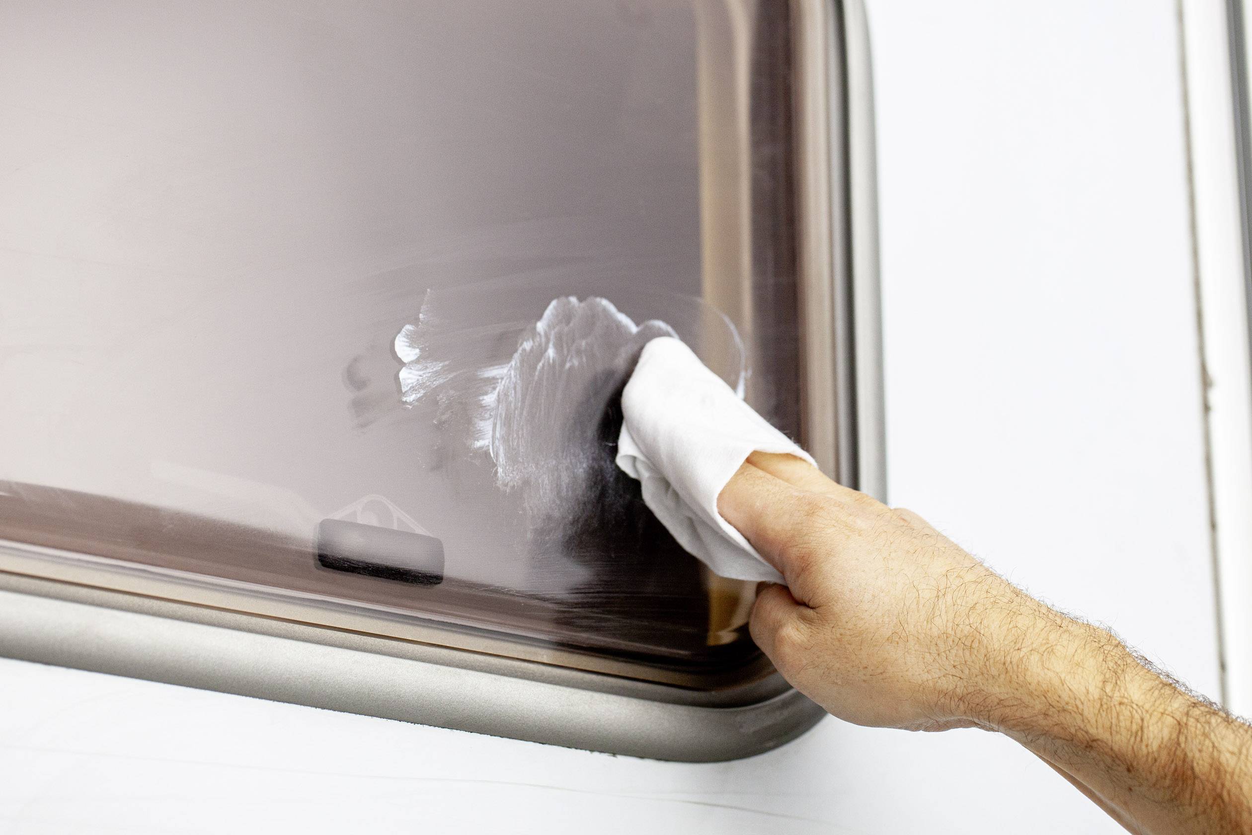 A person is cleaning a window with a white cloth; a wiping motion removes dirt from the smooth surface.
