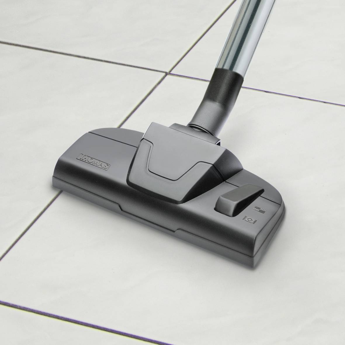 A vacuum cleaner on white tiles shows a close-up of the suction head with a silver tube.