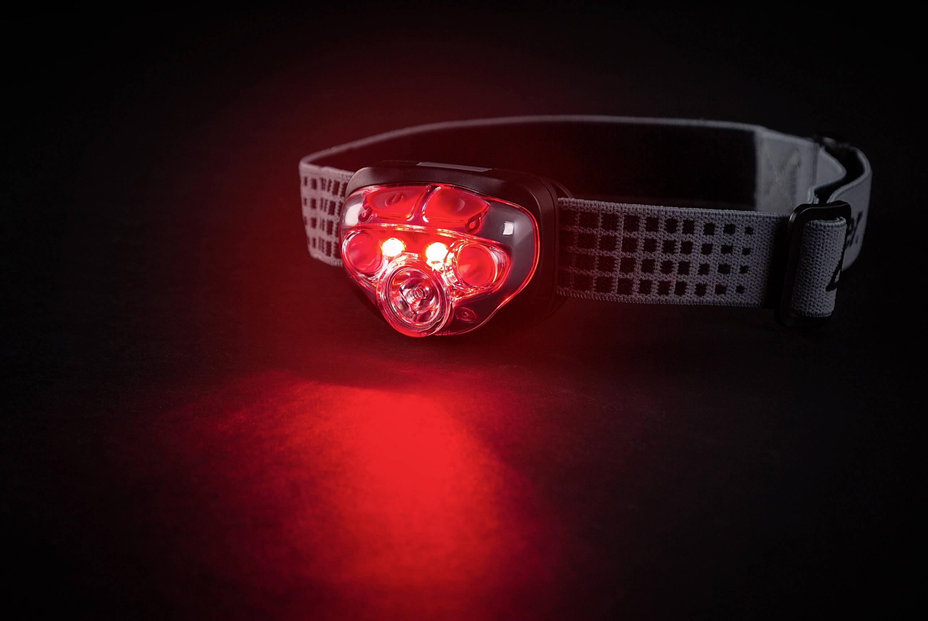 Headtorch with red light on a dark background, shining towards the camera. It is suitable for outdoor activities at night.