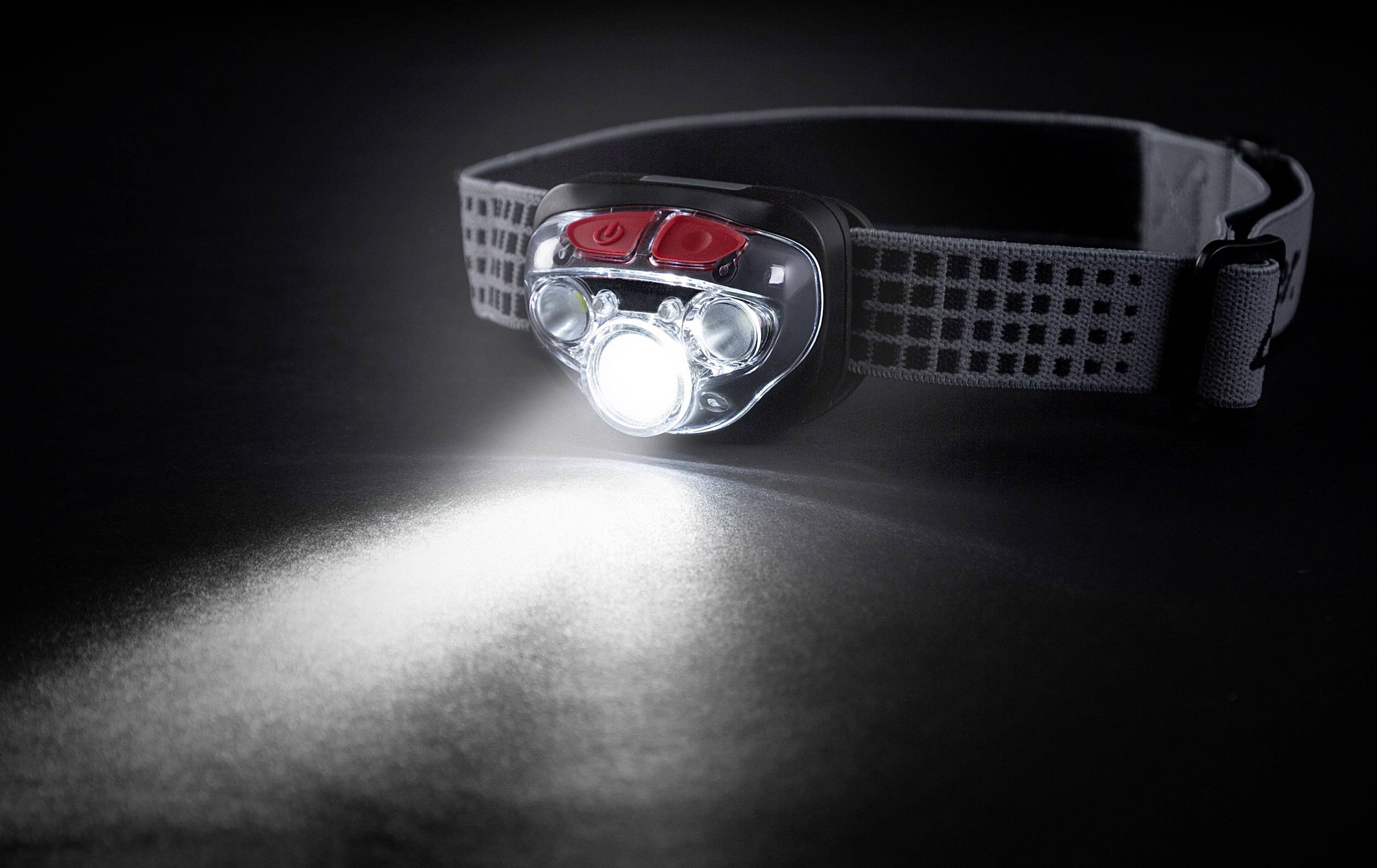 Head torch with bright light beam on dark background, silver strap and red button visible. Ideal for outdoor activities.