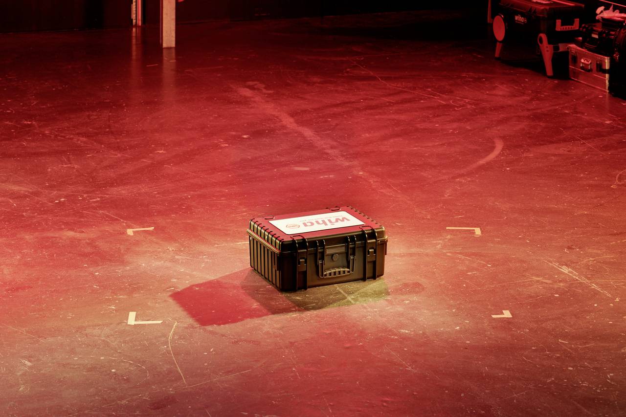 A black transport box with a white and red label on a red stage surface. WDR box for technical equipment.