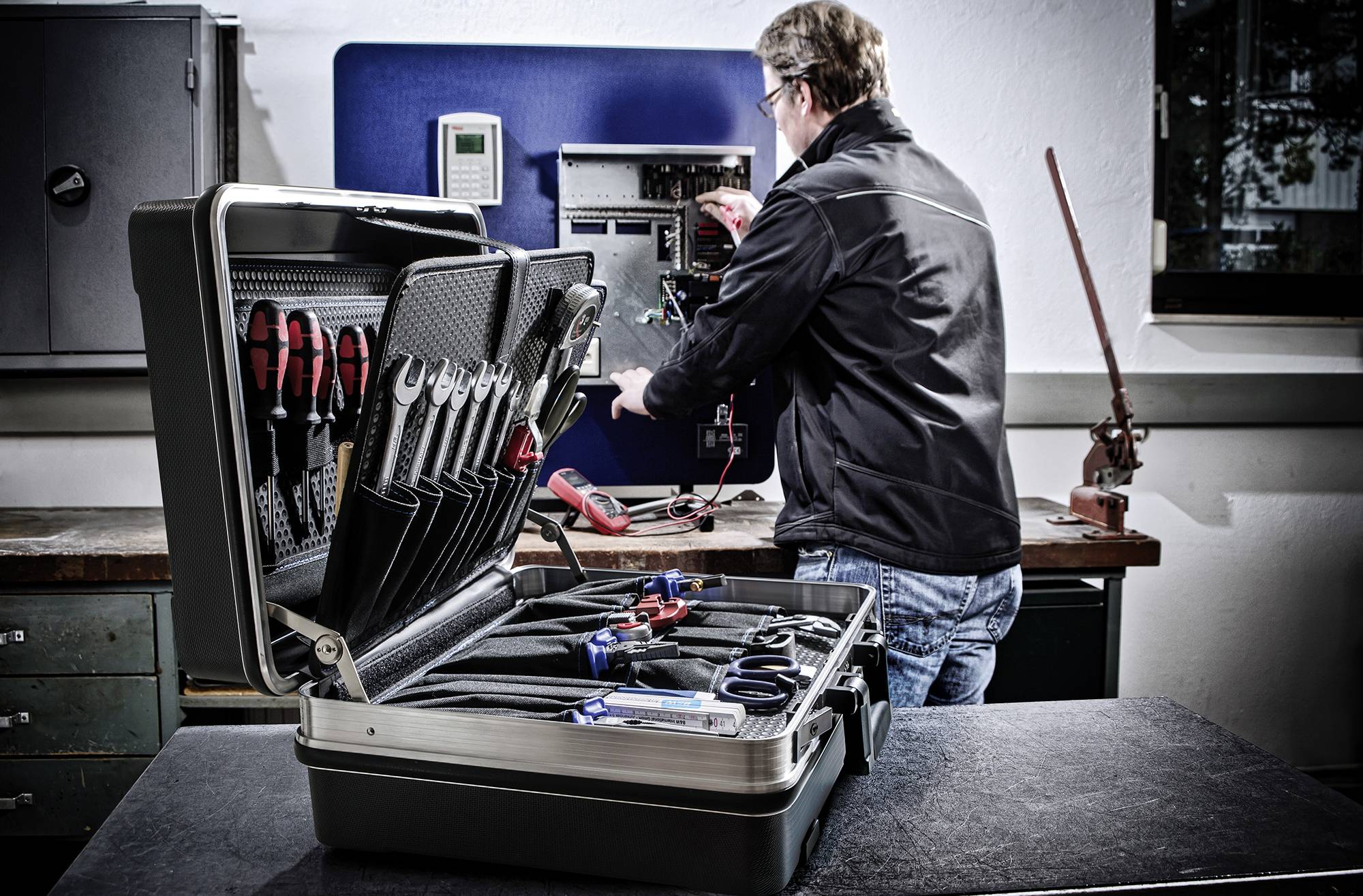 A technician is working on an electrical switchgear, with an open toolbox containing various tools visible in the foreground.