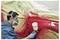 Technician spray-paints a red car panel in a body shop, using a spray gun while the rest of the vehicle is masked with protective plastic and tape.