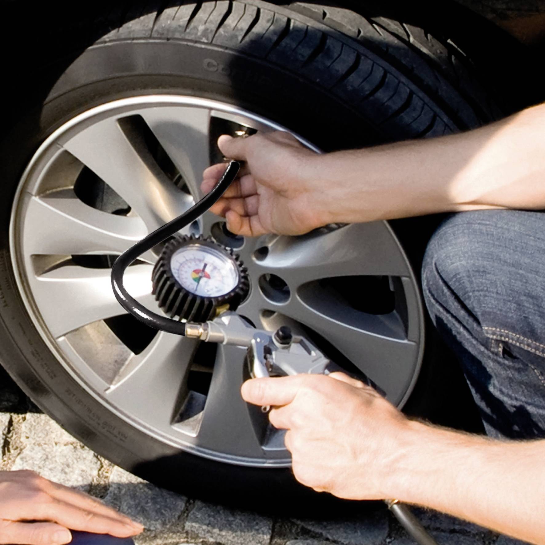 A person is measuring the air pressure of a car tyre with a tyre pressure gauge on a paved road.