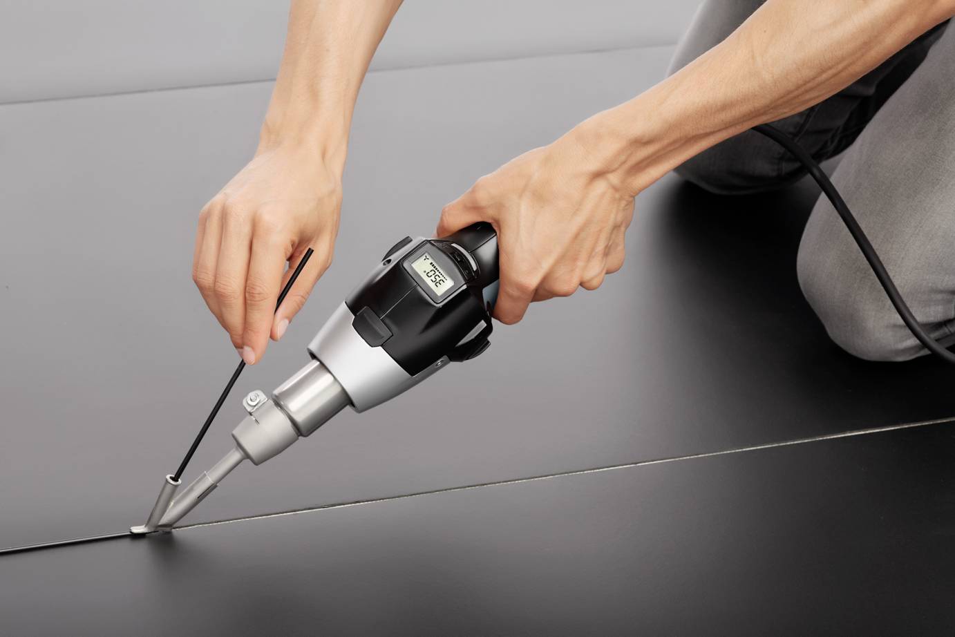 A person is welding two black plastic sheets together using a handheld device and a metal rod, with a focus on precise workmanship.