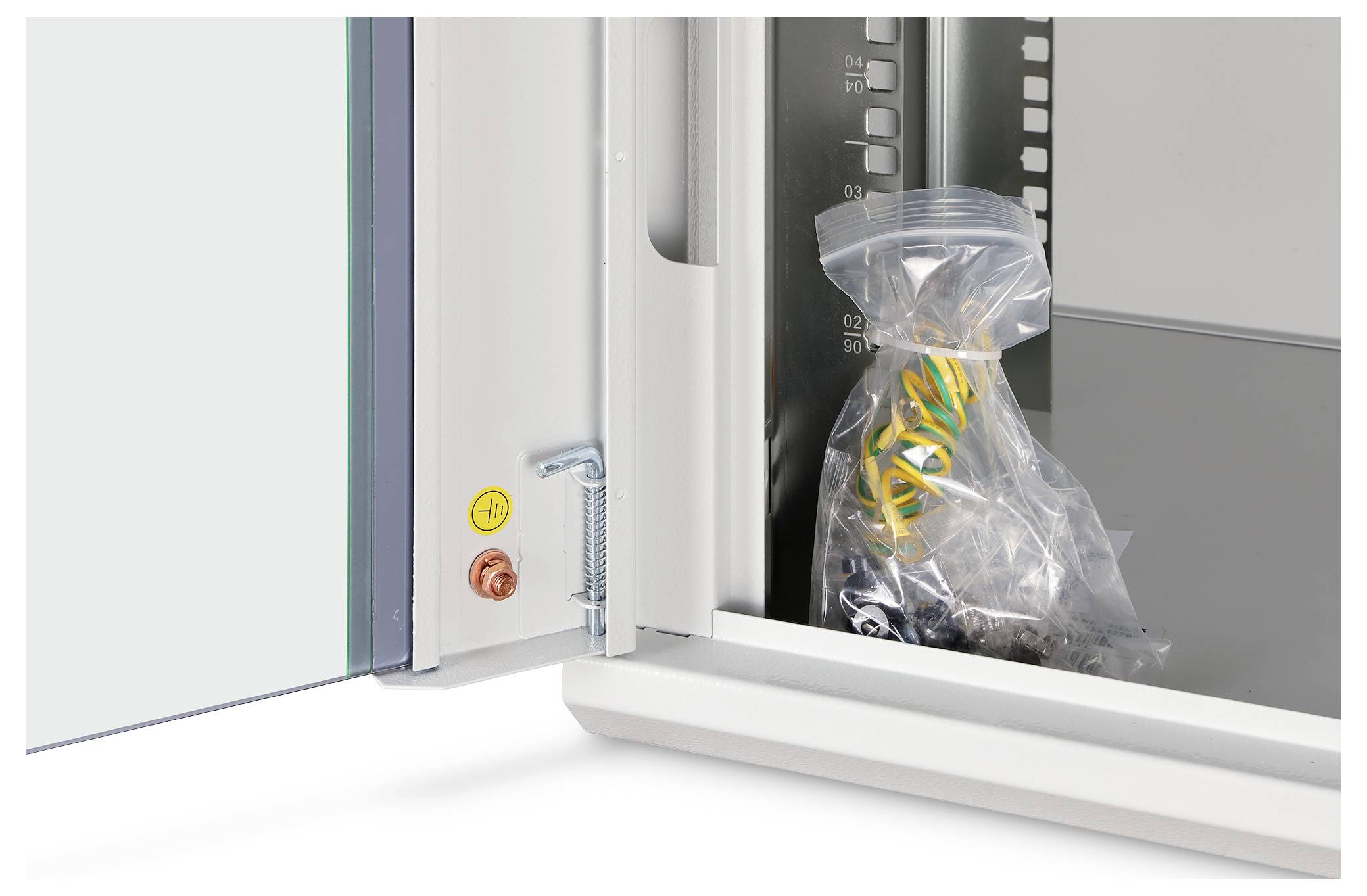 An open cabinet door showing a sealed plastic bag containing yellow and black wires inside the cabinet. A measurement scale is visible on the side.