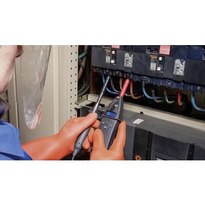 A person wearing protective equipment is measuring the voltage at an electrical switchgear using a multimeter to ensure safety.