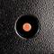 A red button on a black surface with a textured appearance, positioned centrally.