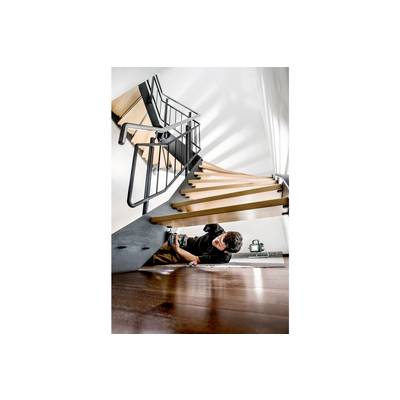 A person is working with a tool beneath a modern wooden and metal staircase. A blank white wall is visible in the background.