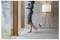 A blurred barefoot person walks past a modern floor lamp in a minimalist room with large glass doors and wood trim.<br>