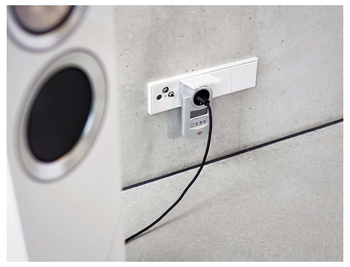 Portable device plugged into a wall outlet on a concrete wall, with a charging cable running to the floor.