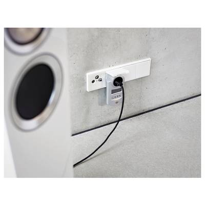 A wall outlet with a plugged-in measuring device and cable beside a speaker, suggesting a power or sound test setup.