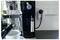 Close-up of a coffee machine plugged into a wall outlet next to light switches, with a cup on the counter in front.