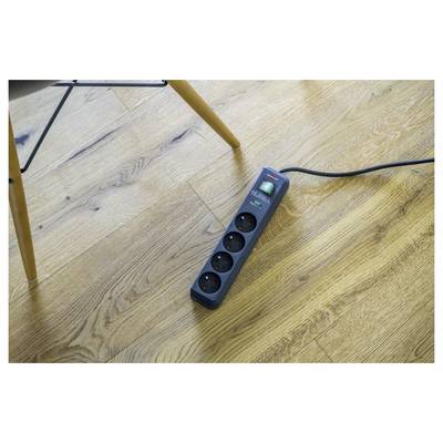 Four-outlet power strip on a wooden floor, with a black cord plugged in and a chair leg nearby.
