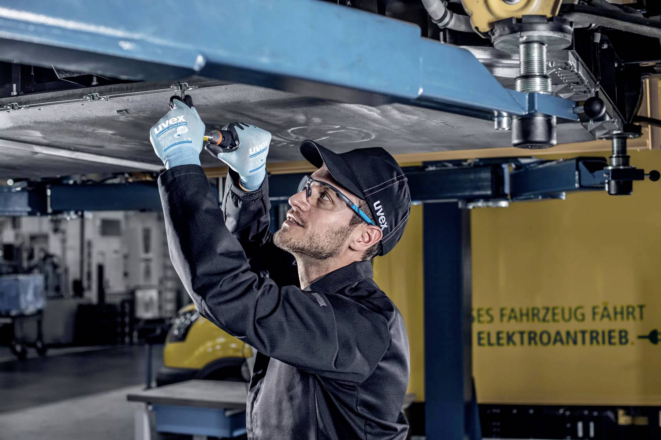 A person in work attire is working underneath a vehicle on a car lift in a workshop.