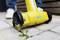 A yellow and blue garden tool removes weeds between paving stones with a rotating brush.