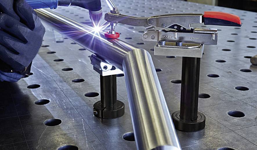 Close-up of a welding process: A worker is welding a metal pipe on a workshop bench.