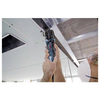 Worker uses a Bosch cordless drill overhead to fasten a ceiling panel in an unfinished interior.