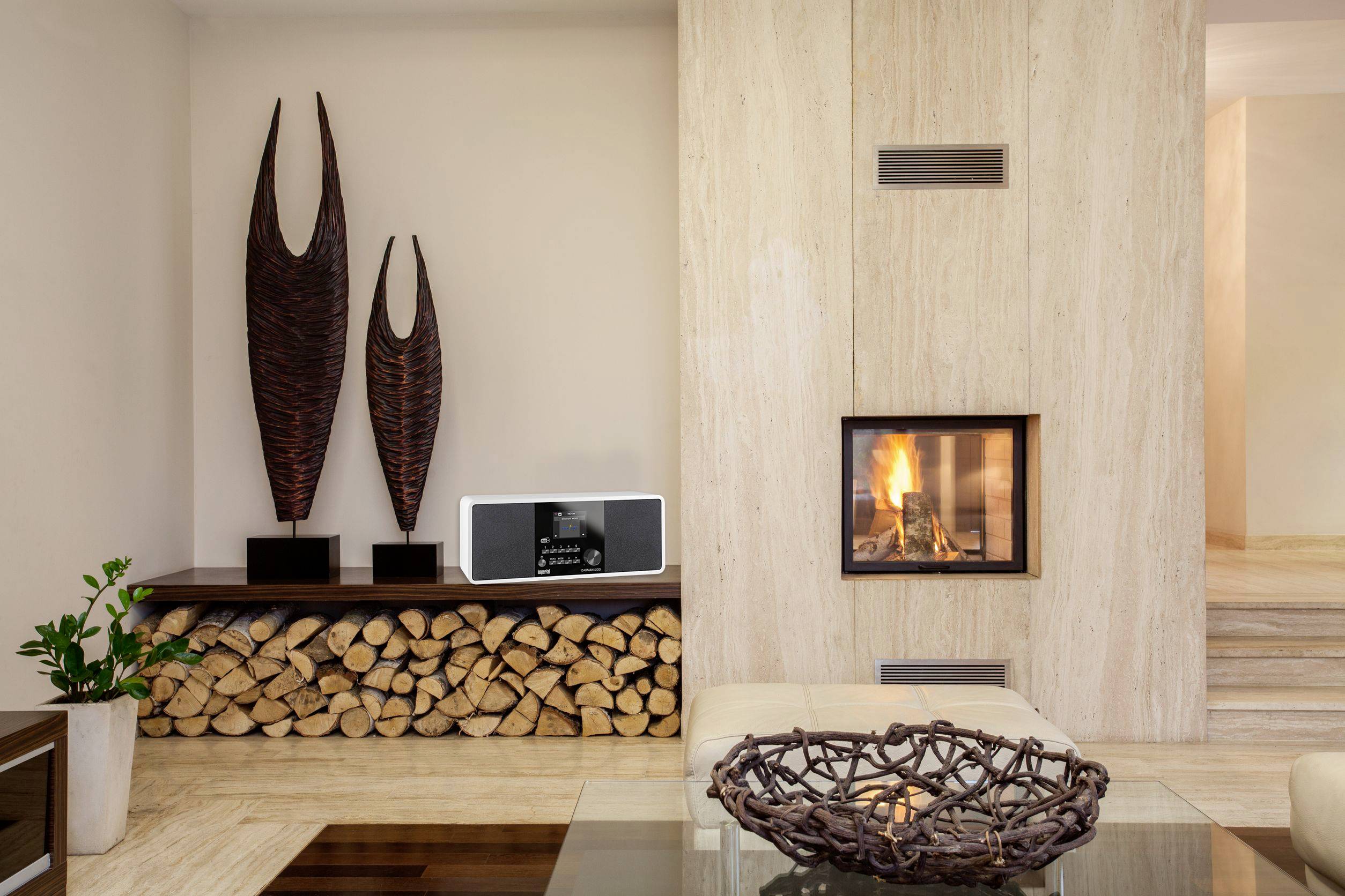 Living room with a modern fireplace, wood pile, sculptures and stereo system, conveying a cosy and stylish atmosphere.
