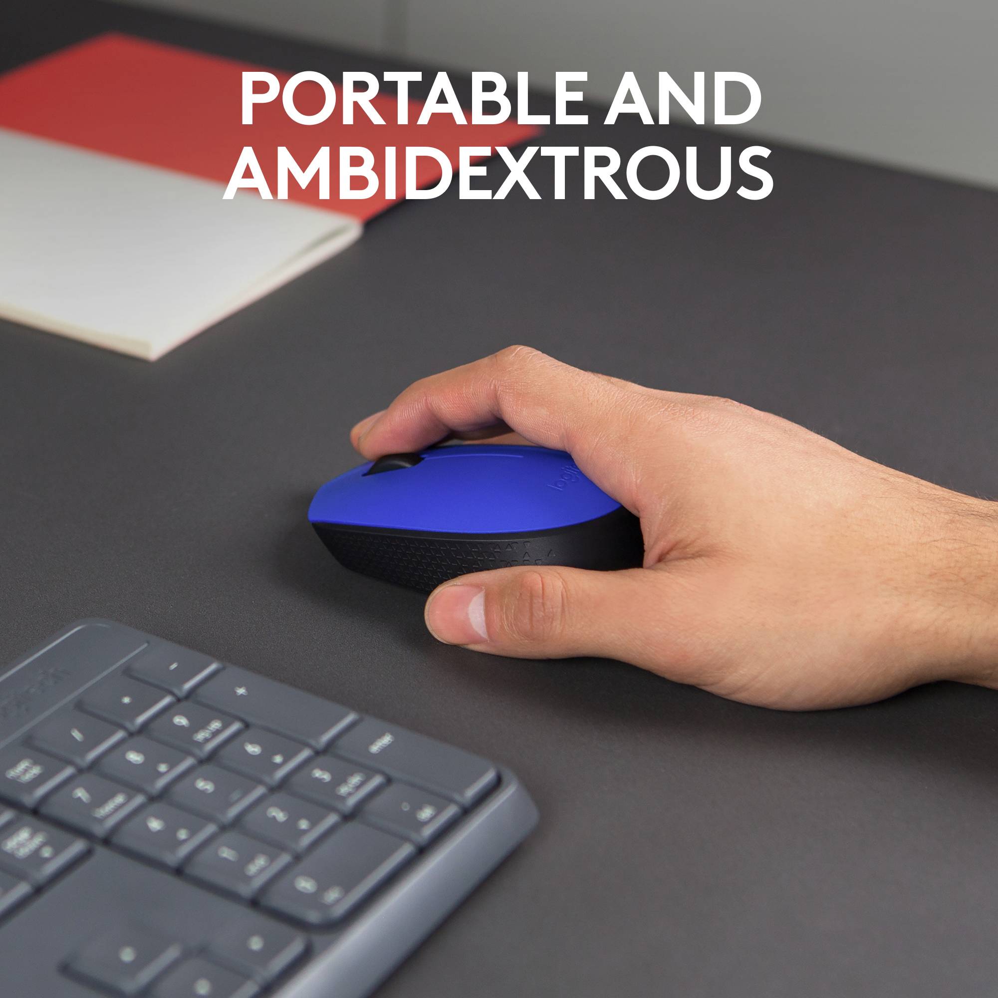 A desk with a keyboard, black and blue compact mouse. A hand is gripping the mouse. Text: 'MOBILE AND OPERABLE WITH BOTH HANDS'.