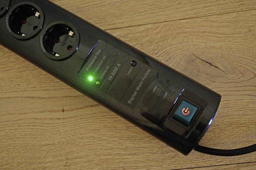 'Power strip with green light on wooden floor, indicating that the power is switched on.'
