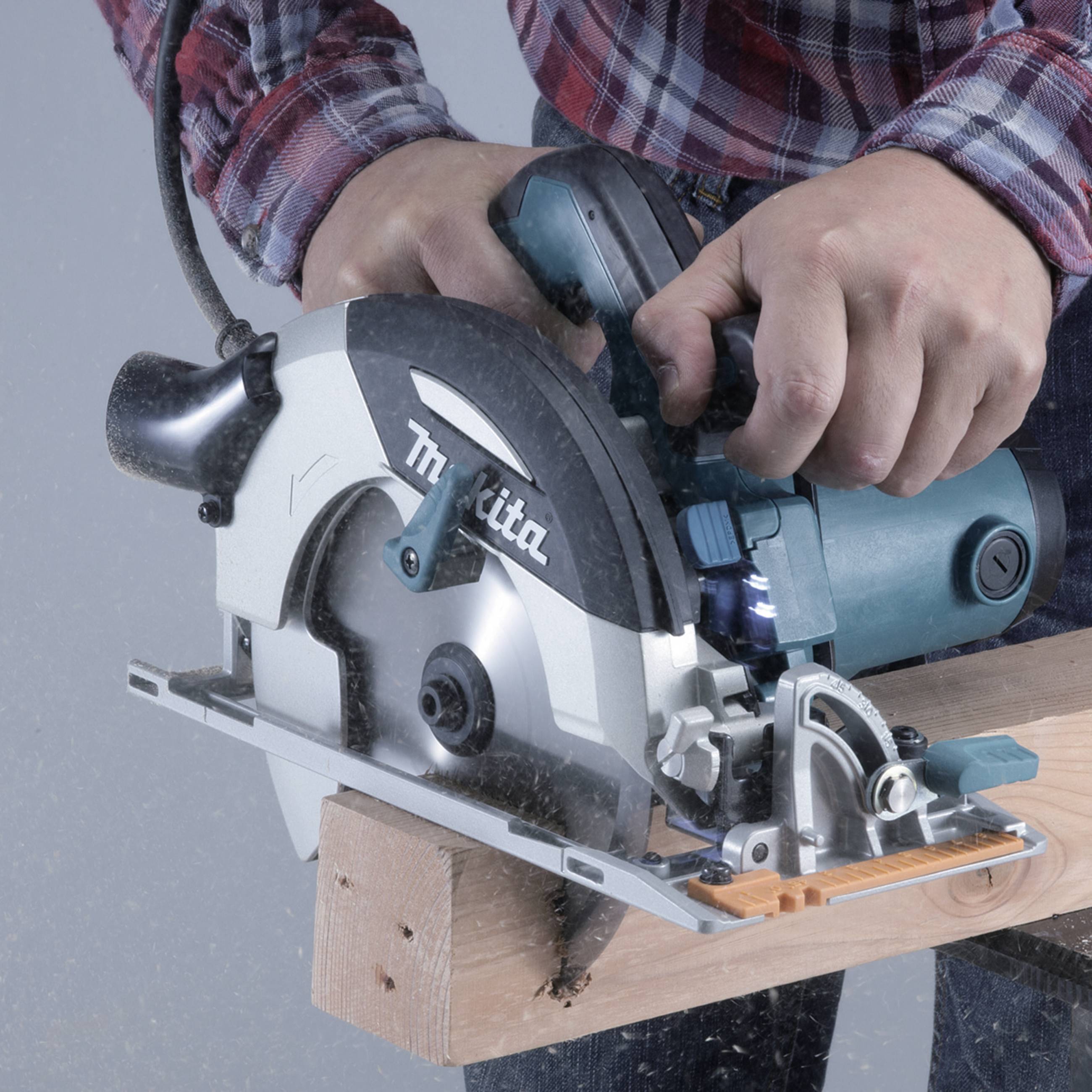 A person is sawing a wooden board with a circular saw. Hands in action. Wood dust visible. No safety precautions apparent.