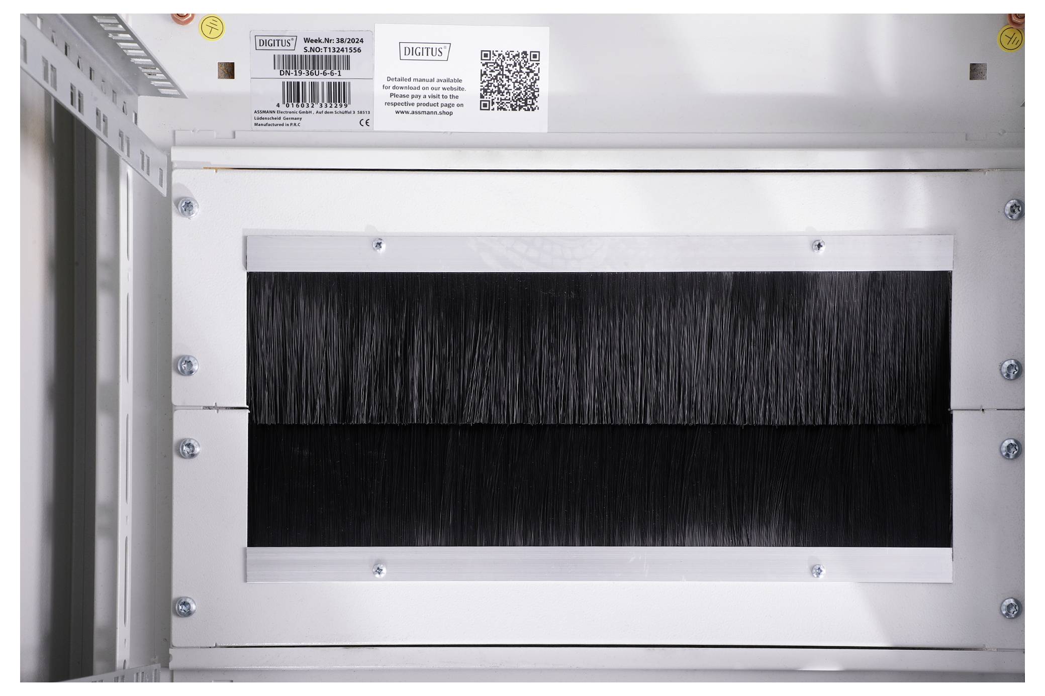 A black cable grommet with brushes in a metallic frame, mounted in a server rack to protect and organise cables.
